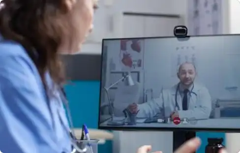 Two doctors communicating through a telemedicine video call on a monitor—highlighting AI-enabled remote healthcare consultations and digital medical collaboration.